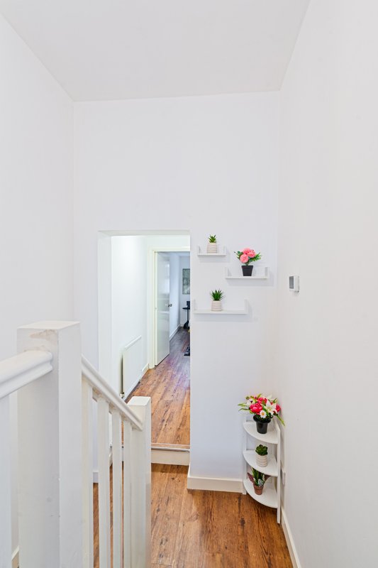 Bright hallway with wooden flooring, white walls, floating shelves with potted plants