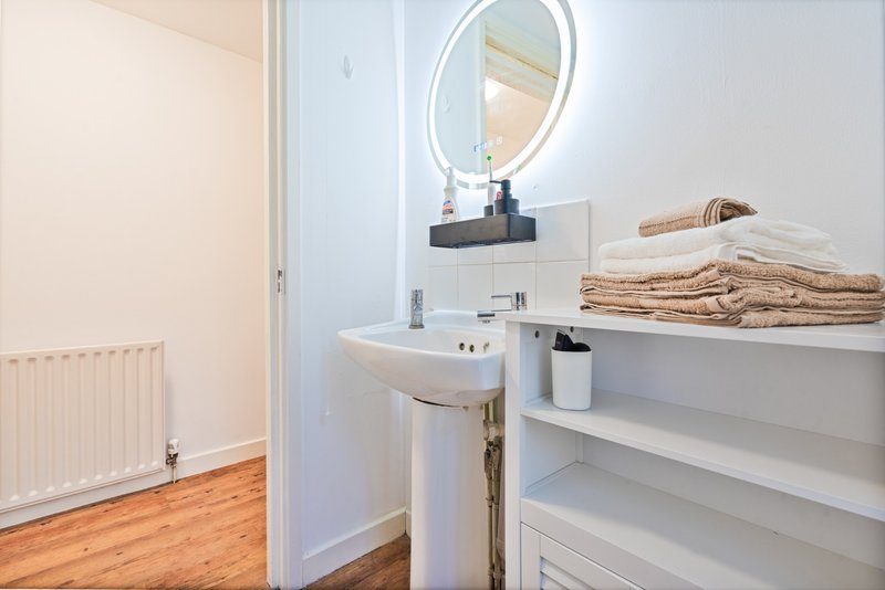 Clean bathroom with wall-mounted sink, round mirror, shelving with towels and toiletries