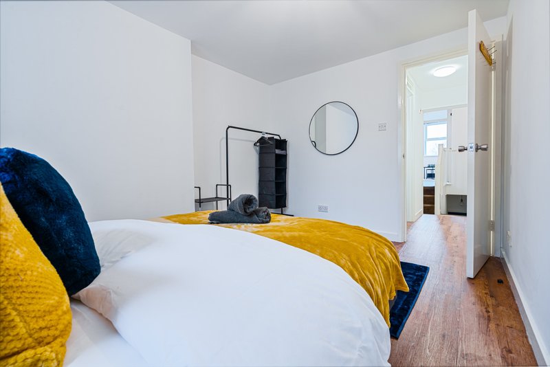 Bright bedroom with double bed, yellow bedding, blue cushions and circular wall mirror