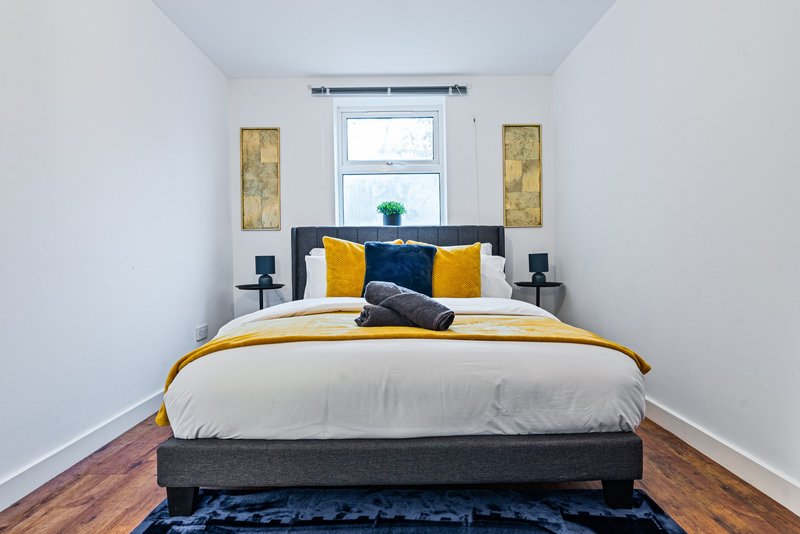 Modern bedroom with double bed, yellow and blue cushions, bedside lamps and window