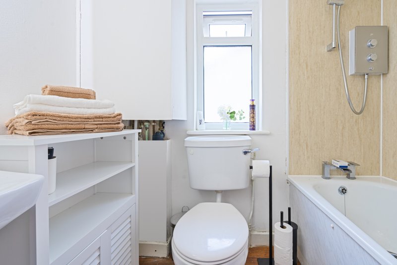 Clean bathroom with toilet, bathtub, white storage shelving and towels