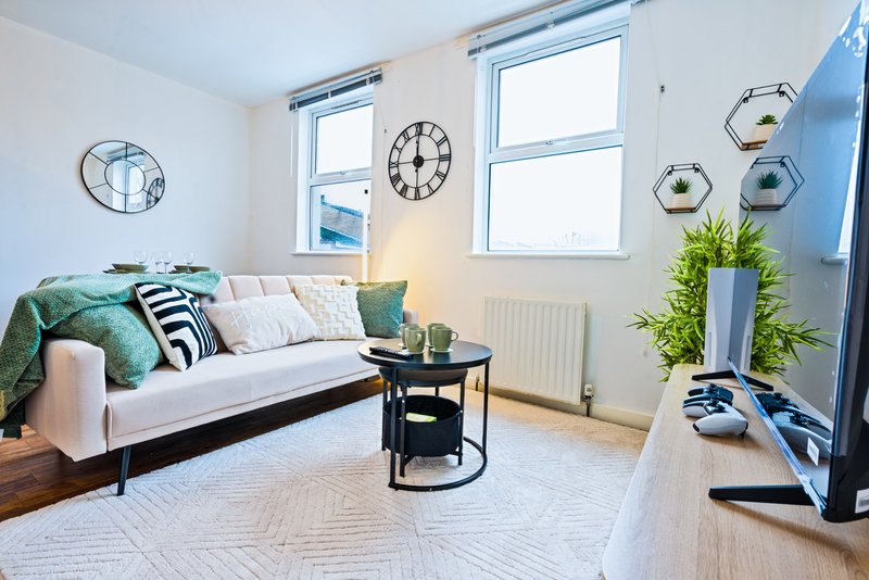 Bright living room with white sofa, decorative cushions, black coffee table, wall clocks, and potted plants