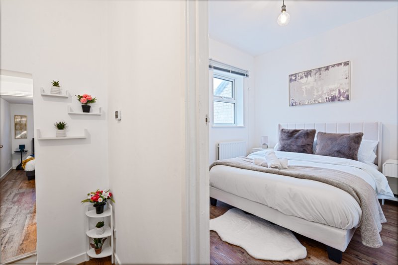 Bright bedroom with white bed, grey pillows, window, floating shelves and potted flowers