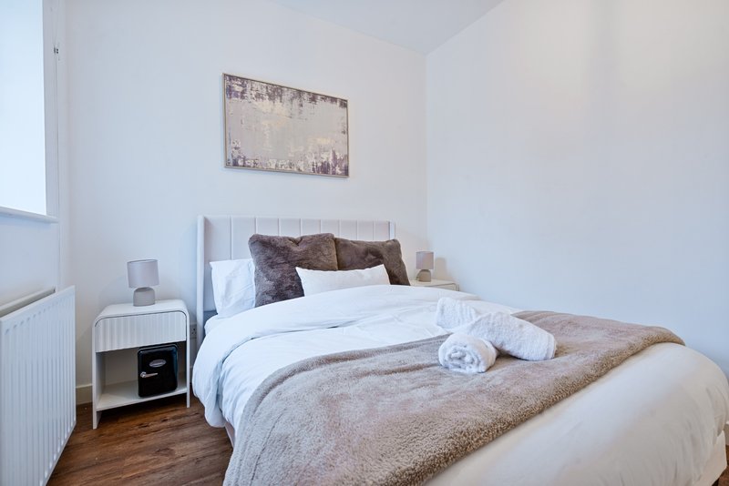 Bedroom with double bed, white bedding, brown throw blanket, and bedside table