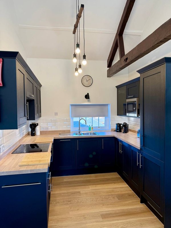 Modern kitchen with dark blue cabinetry, wooden countertops, exposed beams, and coastal view window