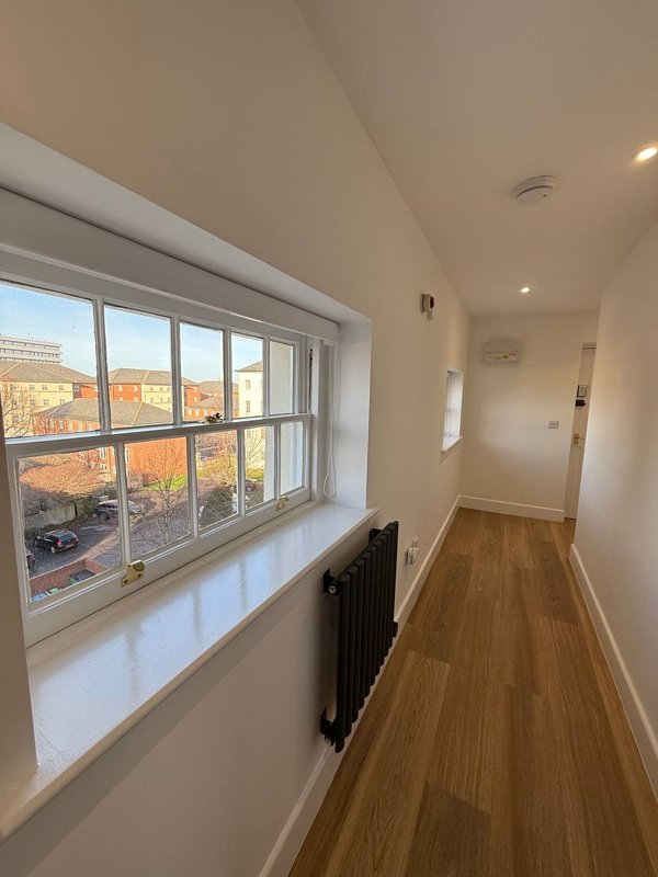 Bright hallway with large window overlooking residential street, wooden flooring and white walls