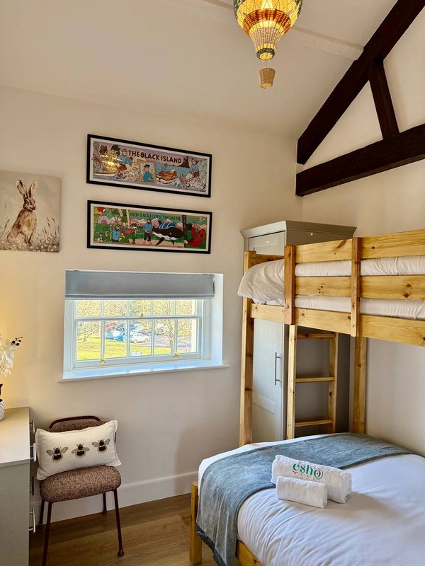 Bedroom with bunk bed, window, framed prints, chair and ceiling light fixture