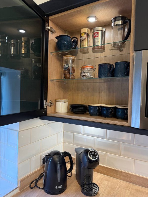 Kitchen cabinet with open doors displaying coffee maker, kettle, mugs, and glasses
