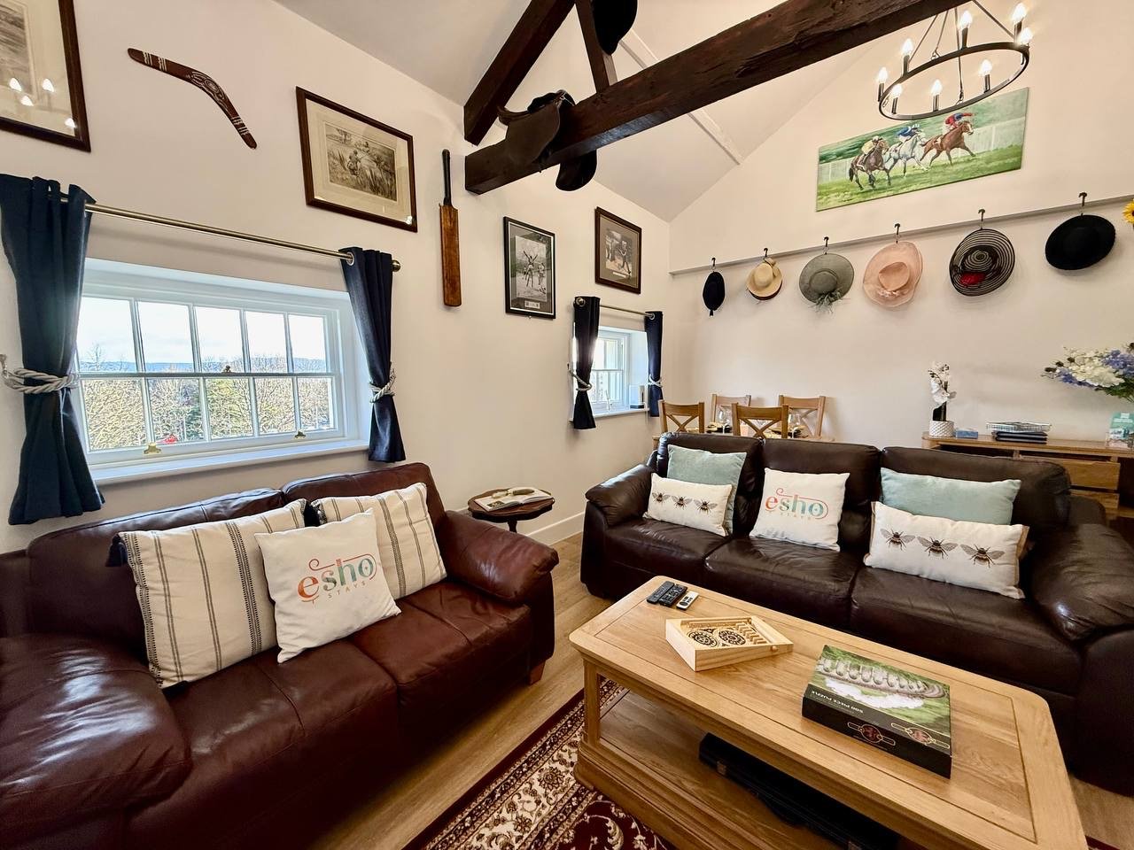 Rustic living room with leather sofas, wooden beams, decorative plates, and countryside views from windows