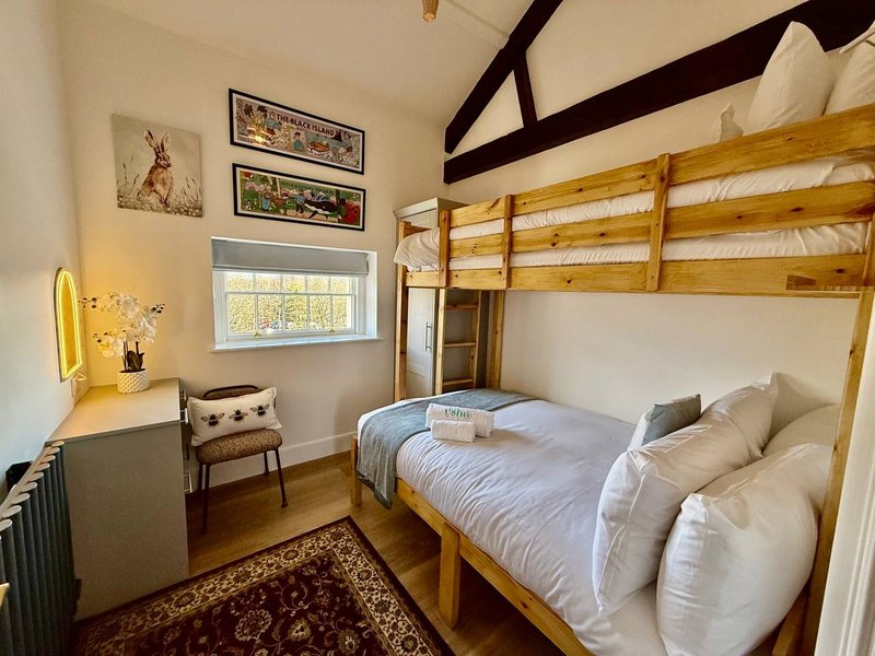 Bedroom with wooden bunk bed, desk with yellow lamp, chair, and window with natural light