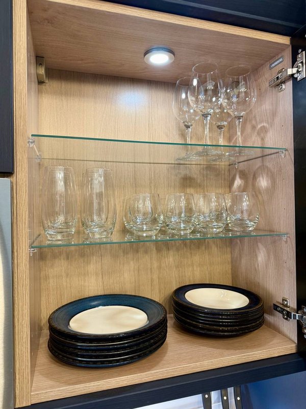 Open wooden cabinet shelves displaying glassware and stacked plates