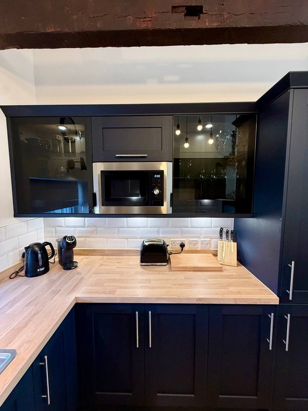 Modern kitchen with dark blue cabinetry, wooden countertop, built-in microwave and white tile splashback