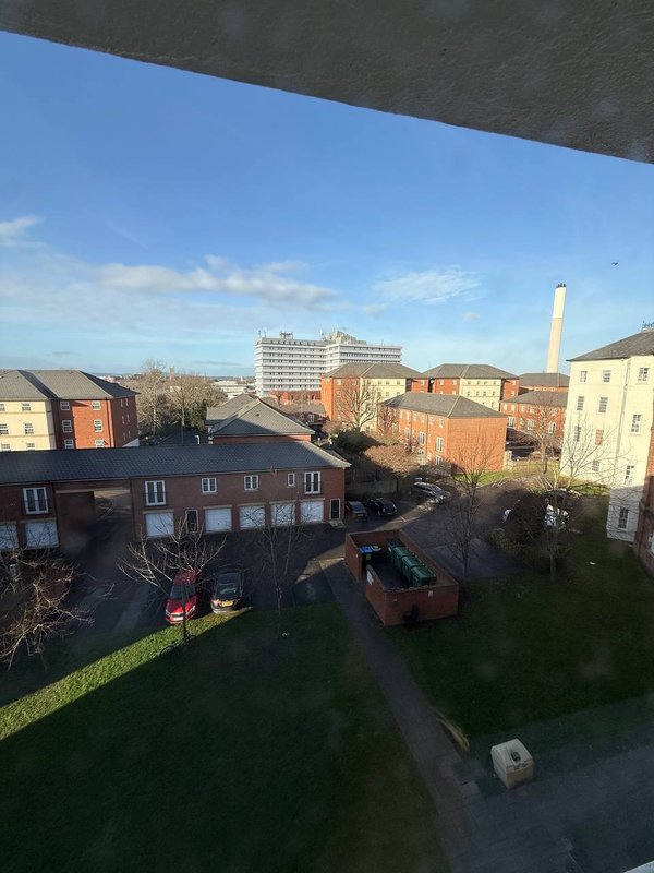 Elevated view of residential street with brick buildings, parked cars, and distant cityscape under clear sky