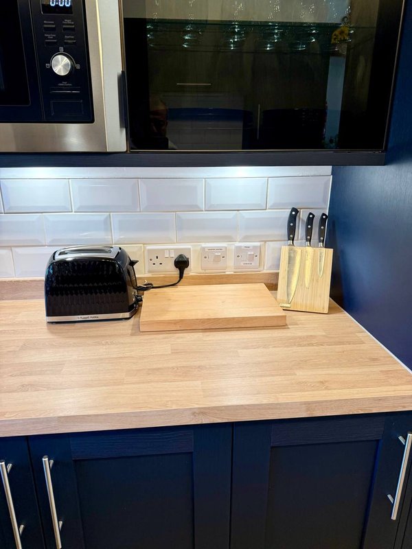 Kitchen countertop with black toaster, wooden knife block, and wall-mounted outlets above white tile backsplash