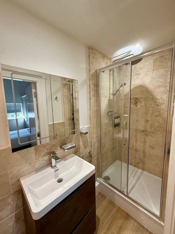 Modern bathroom with white sink, glass shower enclosure, and travertine tile walls