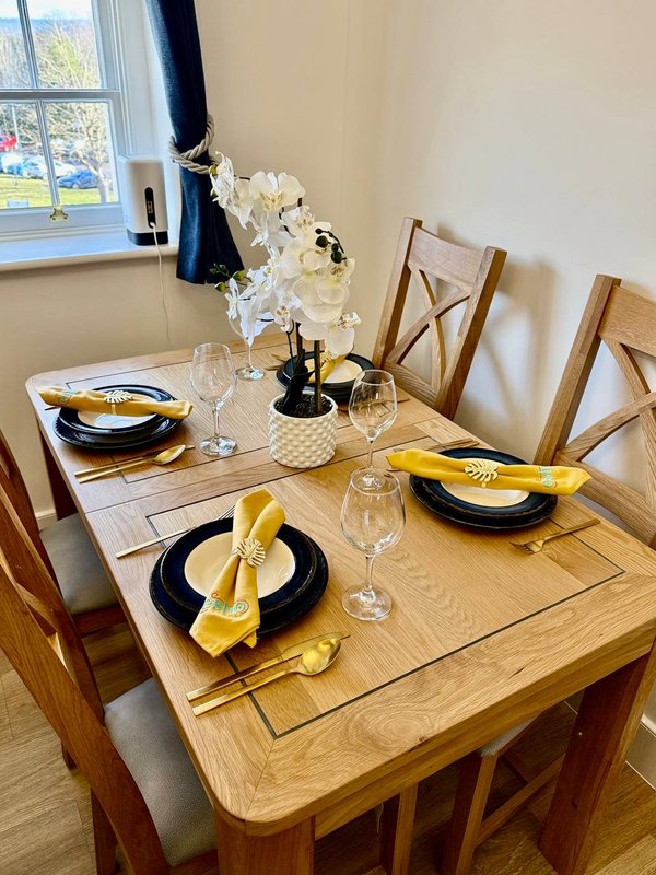 Dining room with wooden table set for four, black plates, yellow napkins, and white orchid centerpiece
