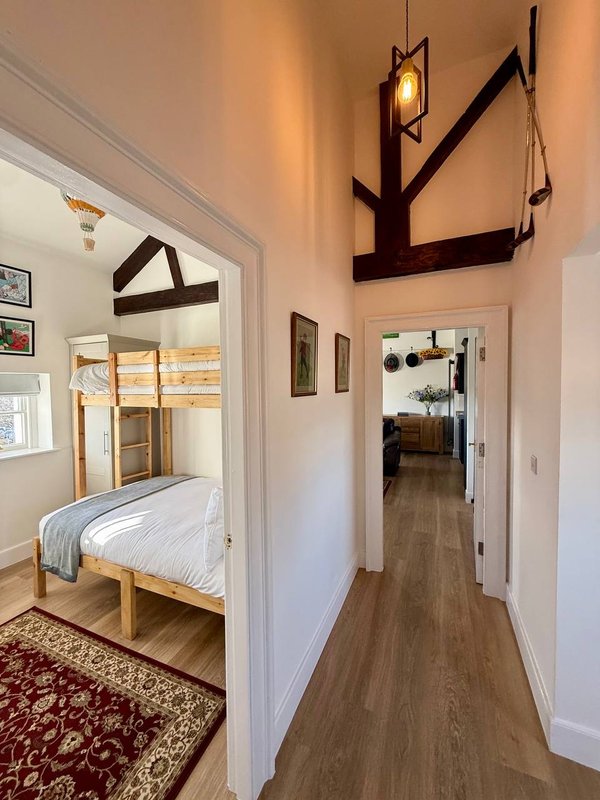 Hallway with wooden floors, white walls, and open doorway to bedroom with wooden bed frame