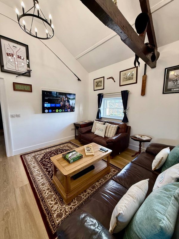 Living room with leather sofa, wooden coffee table, wall-mounted TV, and exposed wooden beam ceiling