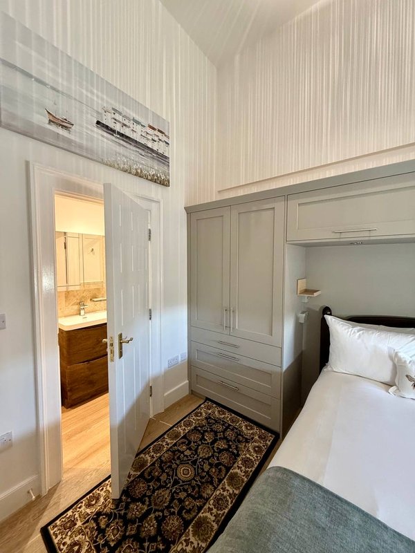 Bright bedroom with white bed, built-in wardrobe, open door to ensuite bathroom