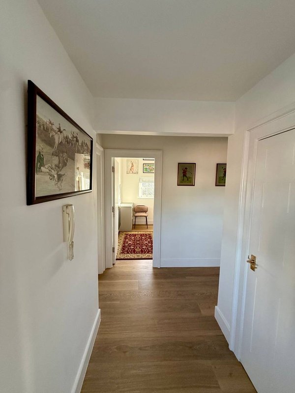 Bright hallway with wooden floor, framed wall art, and open doorway to living area