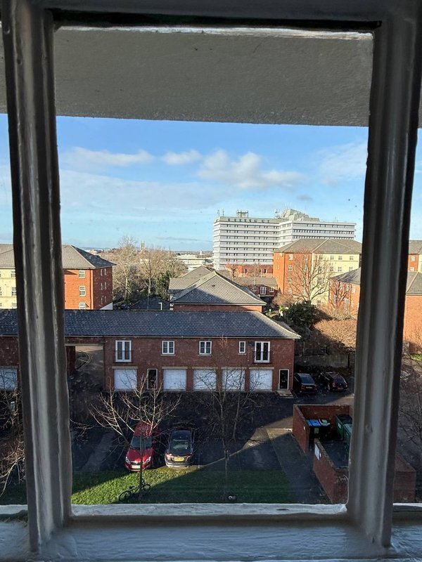 Window view of urban street with brick buildings, parked cars and blue sky