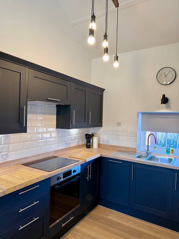 Modern kitchen with dark blue cabinetry, wooden countertops, white subway tile backsplash and pendant lights