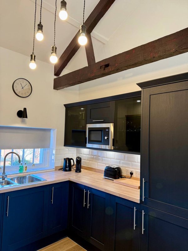 Modern kitchen with dark blue cabinetry, wooden countertop, exposed beam ceiling and pendant lights