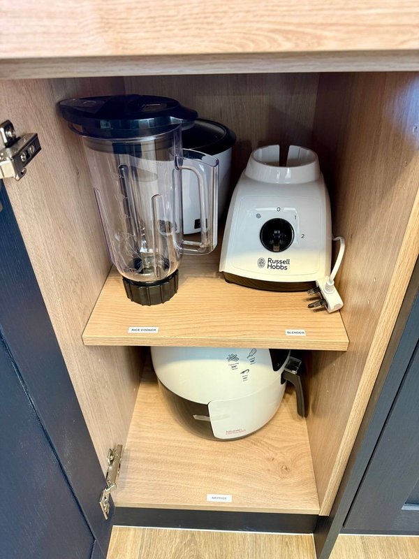 Kitchen cupboard interior with blender, food processor, and white kettle on wooden shelves