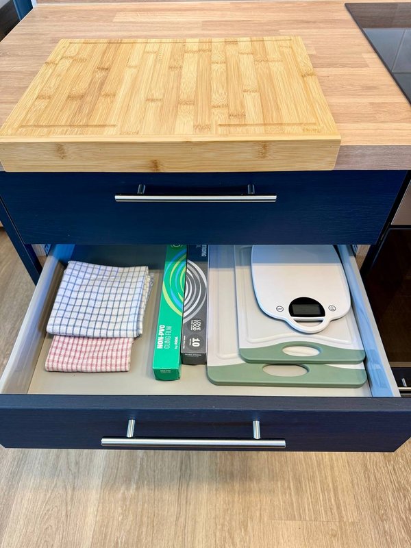 Kitchen drawer open showing organized utensils, cloths, and household items in wooden counter