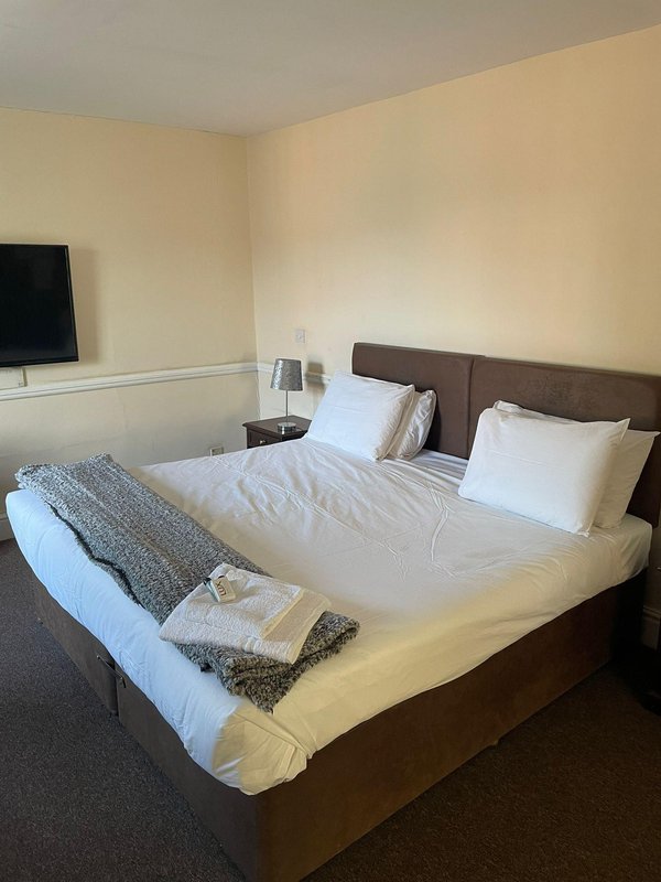 Bedroom with double bed, brown headboard, white bedding, folded towels, and wall-mounted TV.