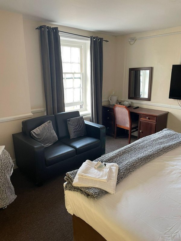 Spacious bedroom with double bed, black leather sofa, desk, window with blue curtains