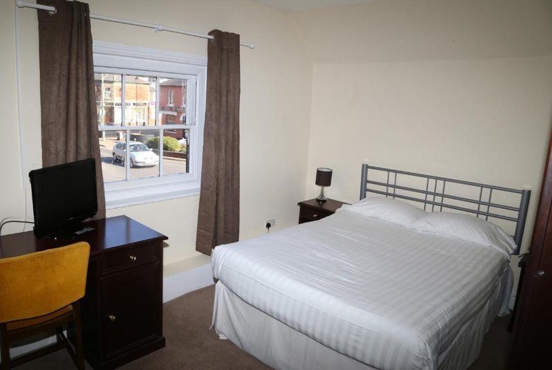 Bedroom with double bed, desk, TV, and window with brown curtains