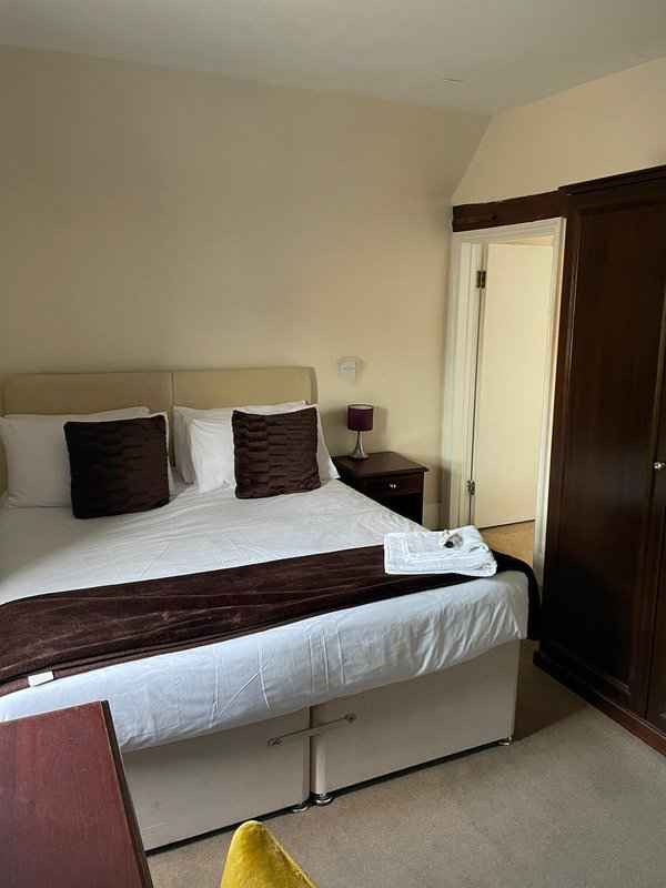 Bedroom with double bed, dark wood headboard, brown cushions, bedside table and dark wardrobe.