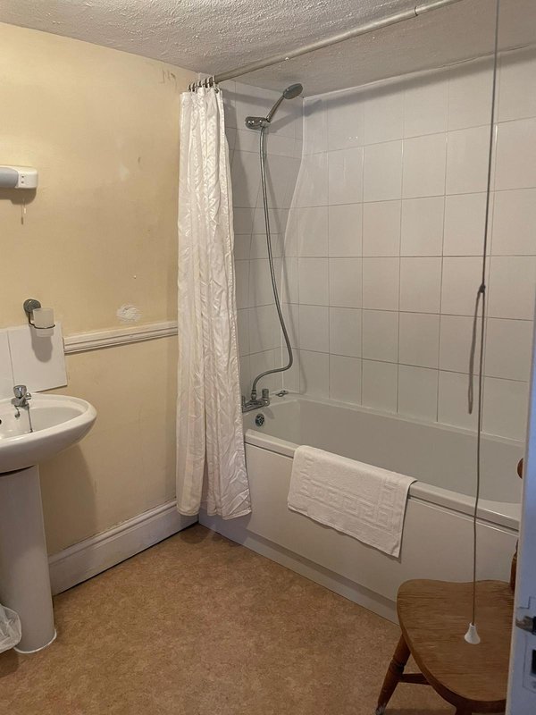 Bathroom with pedestal sink, bathtub with shower screen, and white tile walls