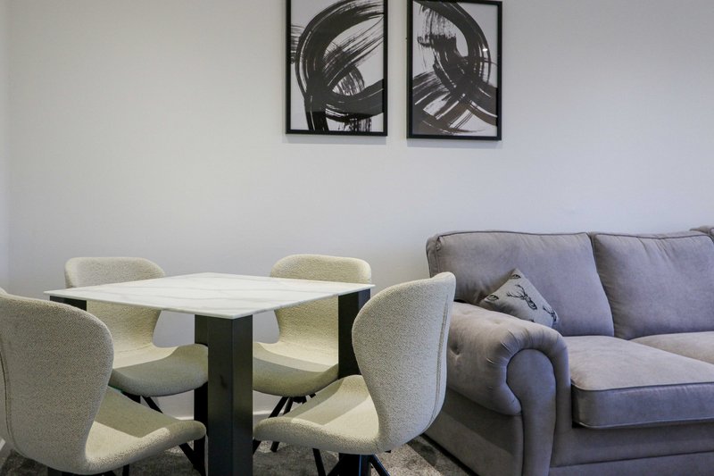 Modern living space with dining table, upholstered chairs, sofa and abstract wall art