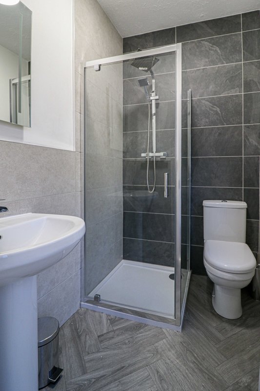 Modern bathroom with gray tile walls, glass shower enclosure, white sink and toilet