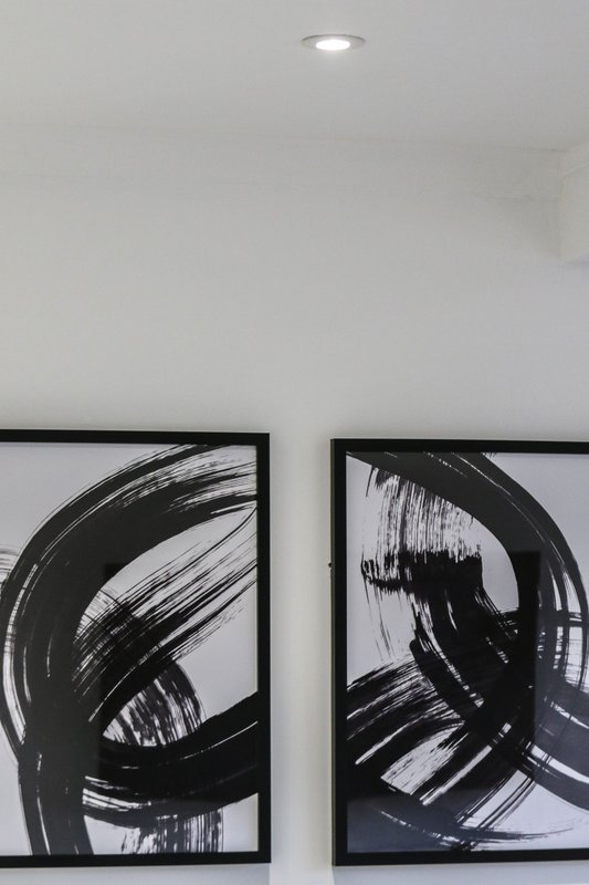 Two framed abstract black and white artworks on white wall with recessed lighting
