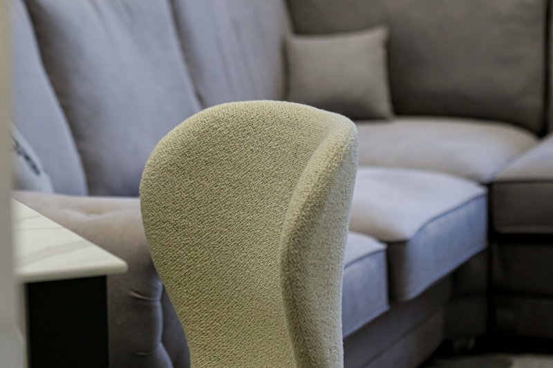 Close-up of cream upholstered armchair with gray sofa and cushions in background