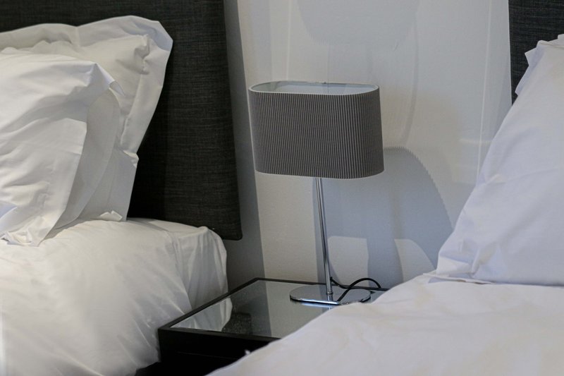Bedroom with two beds, white pillows and bedding, dark headboard and grey table lamp