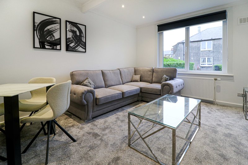 Modern living room with grey corner sofa, glass coffee table, dining chairs and abstract wall art