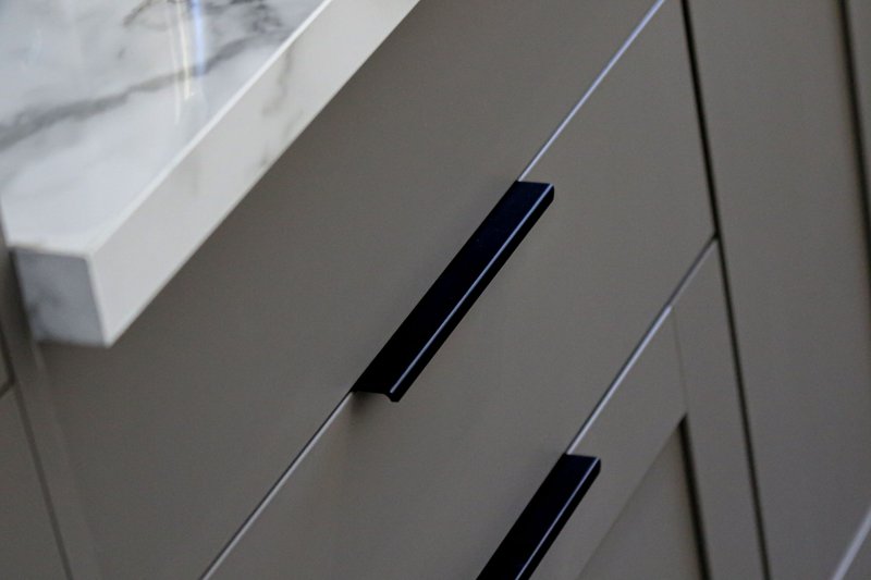 Close-up of modern gray kitchen cabinetry with black metal handles and white countertop