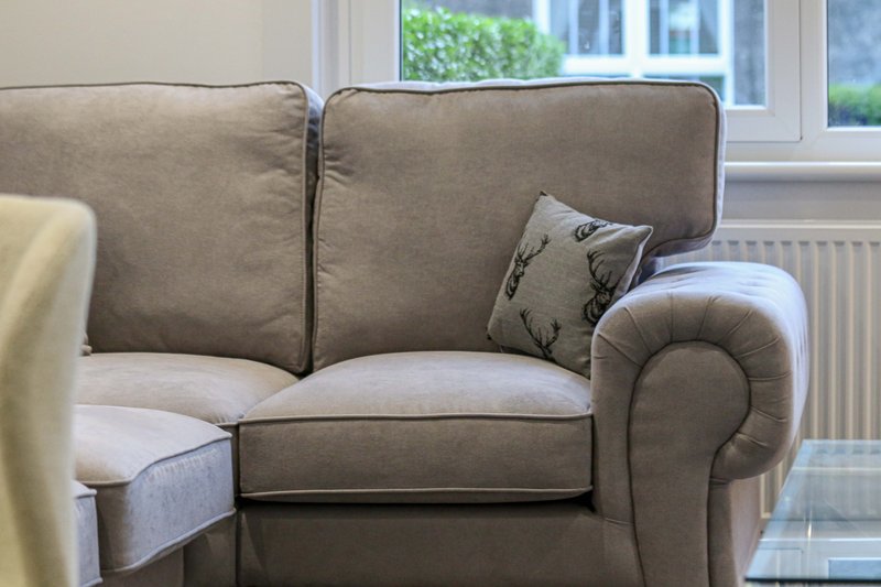 Beige upholstered sofa with rolled arms and decorative cushions near bright window