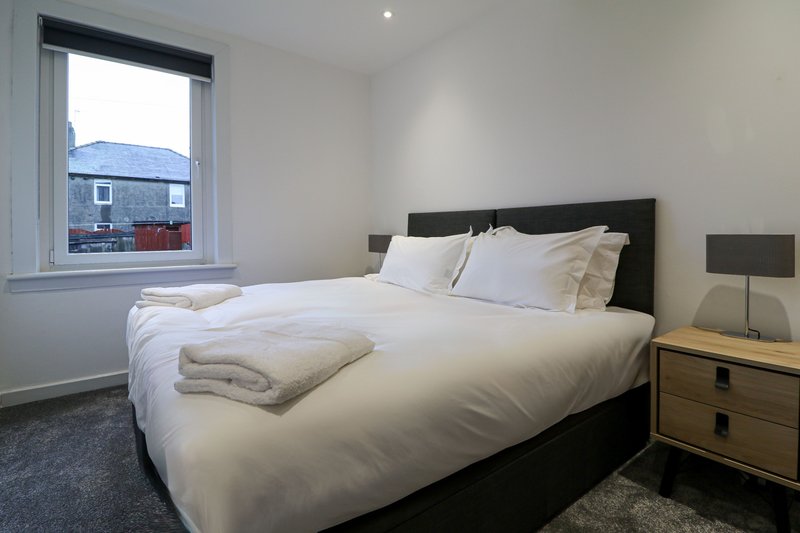 Bright bedroom with double bed, black headboard, wooden nightstand and window view