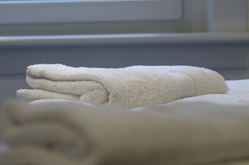 Folded cream towels stacked on bed with headboard in background