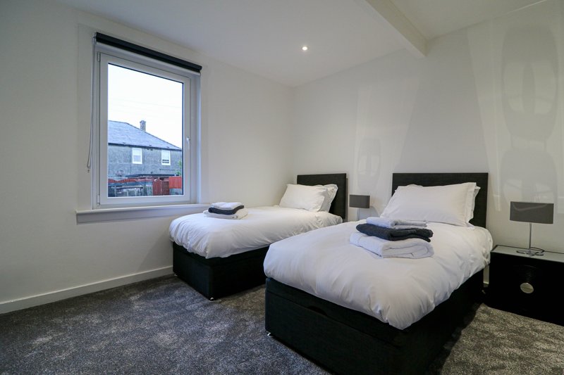 Twin bedroom with two single beds, black frames, white bedding, and window view