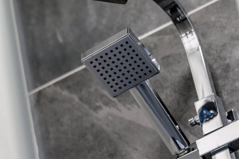 Modern chrome shower head with rainfall nozzle mounted on tiled bathroom wall