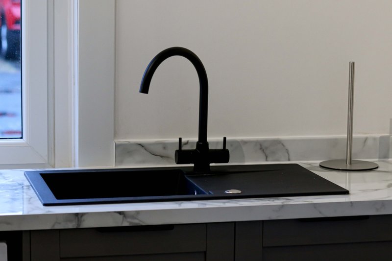 Modern kitchen sink with black tap, marble countertop and window view