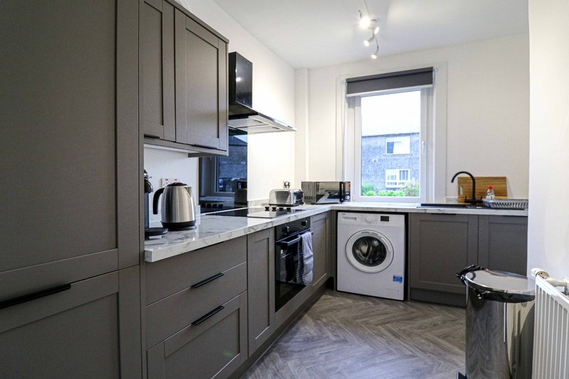Modern kitchen with grey cabinetry, integrated appliances, washing machine and window view