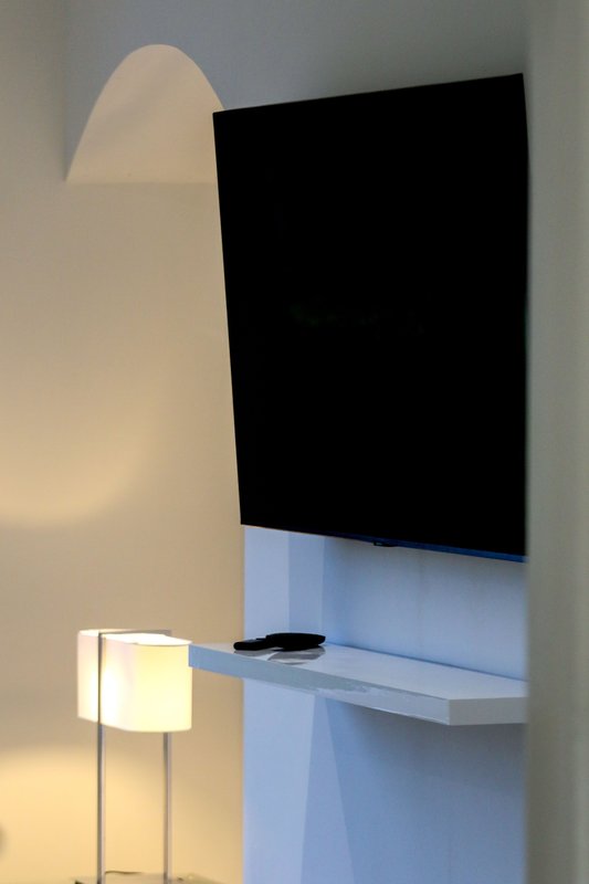 Modern bedroom corner with wall-mounted TV, white floating desk, and floor lamp