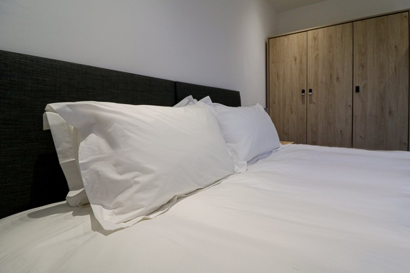 Bedroom with white bedding, black headboard, and wooden wardrobe doors